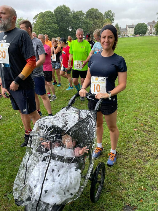 photograph of a woman at the start line of a running race with a baby in a running buggy. She is wearing a race number