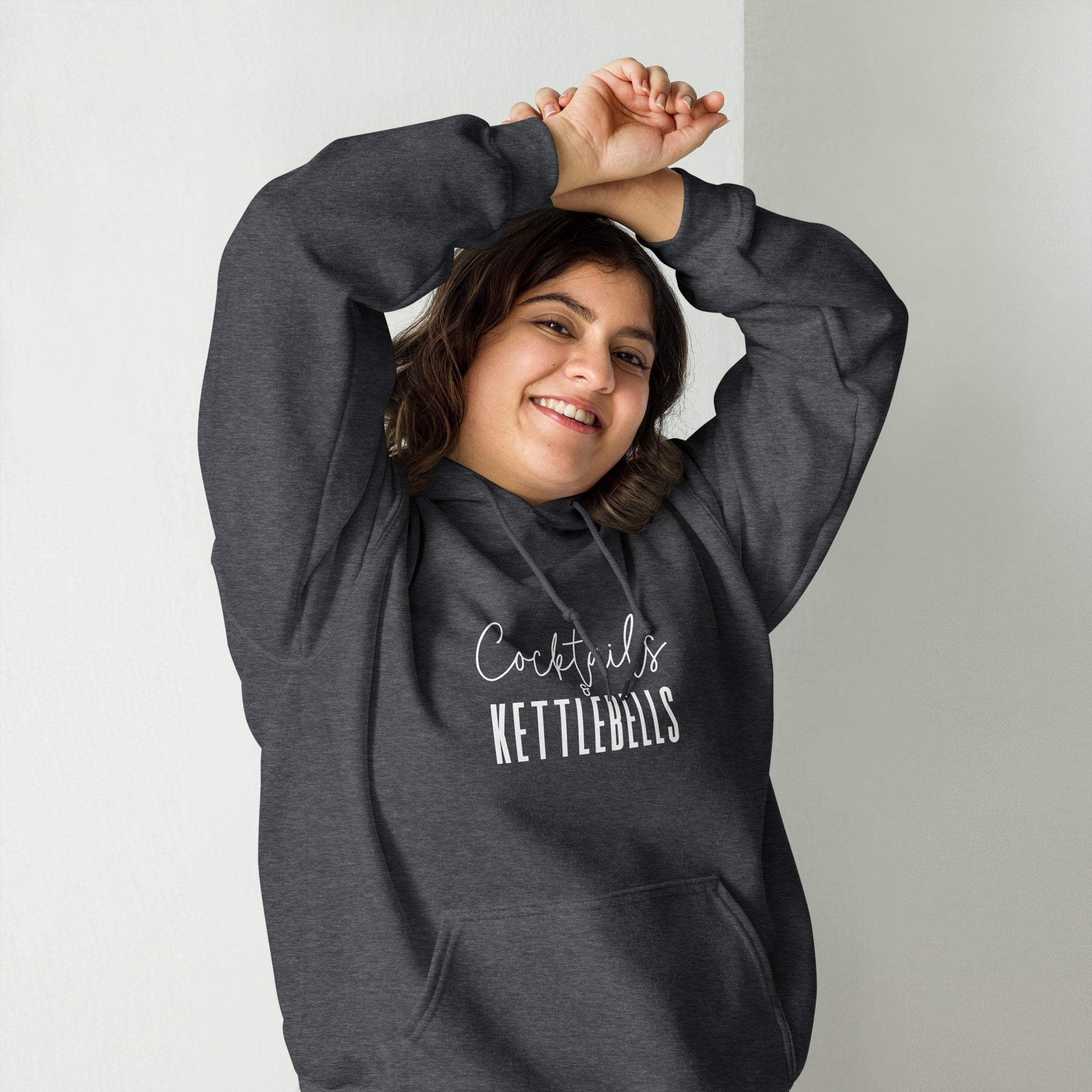 woman wearing a grey hoodie with the words cocktails and kettlebells in a white font across the chest