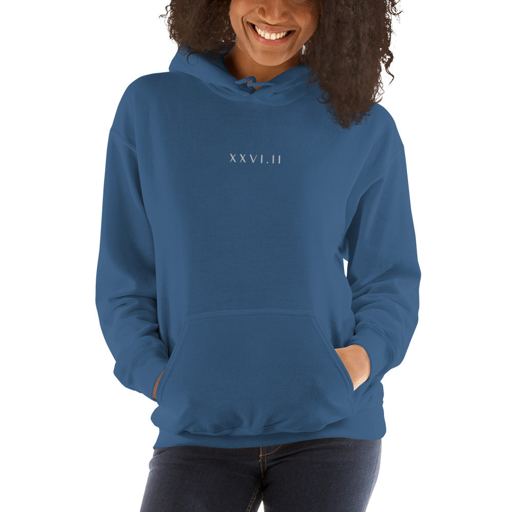 woman wearing a dusky blue hoodie with XXVI.II 26.2 marathon distance in roman numerals in a small, white font embroidered across the chest